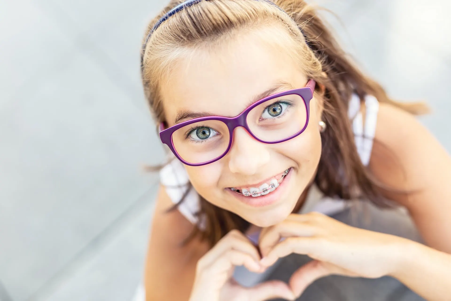 Smiling girl with braces and glasses making a heart with her hands