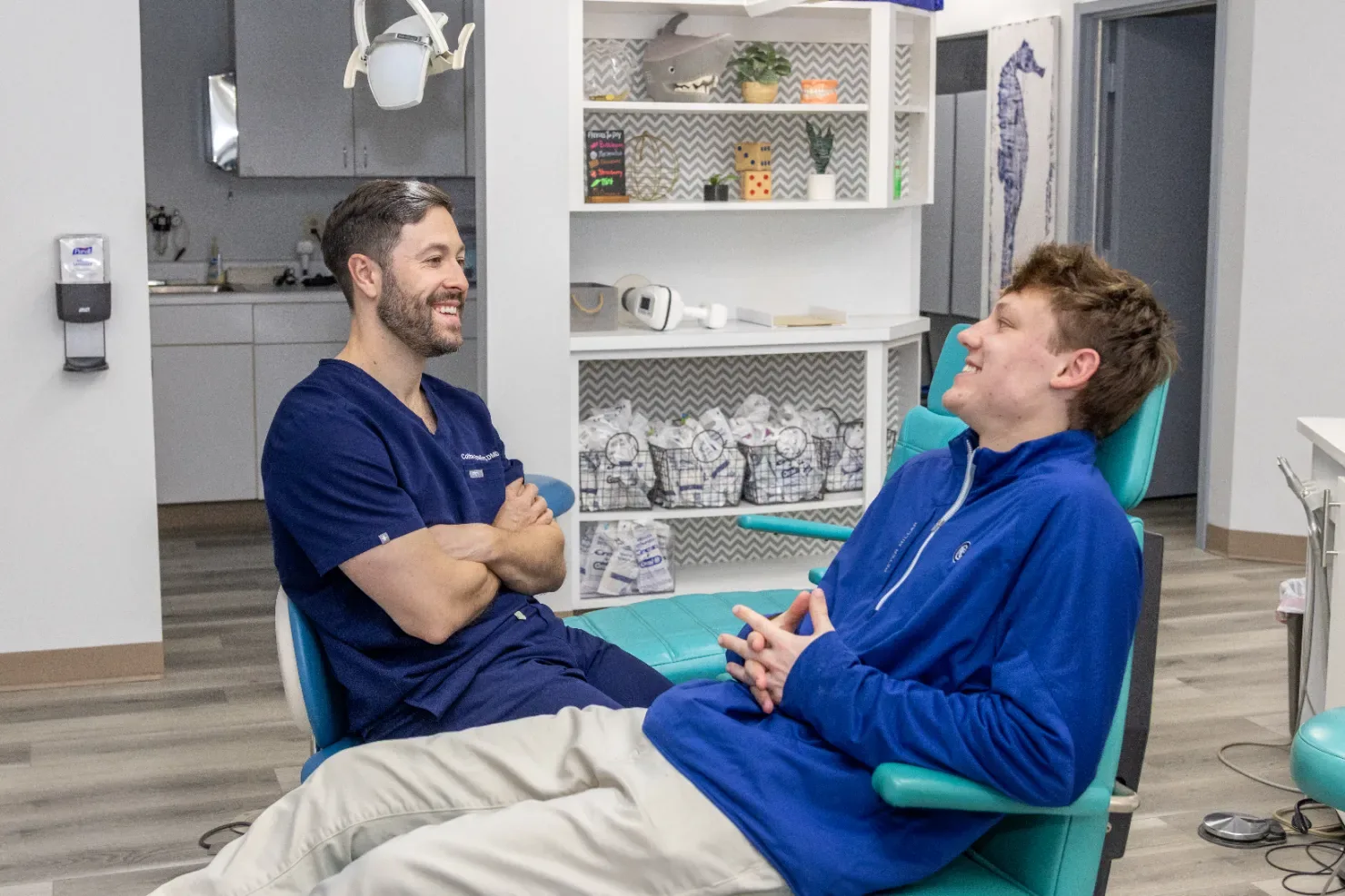 A dentist chatting with a smiling teen patient in a treatment chair